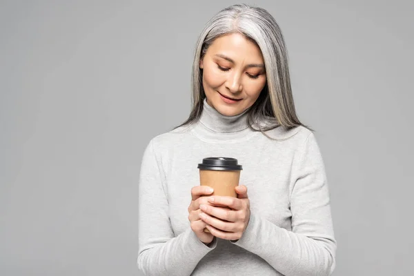 Приваблива азіатська жінка в горлиці з сірим волоссям тримає каву, щоб піти ізольовано на сірому — стокове фото