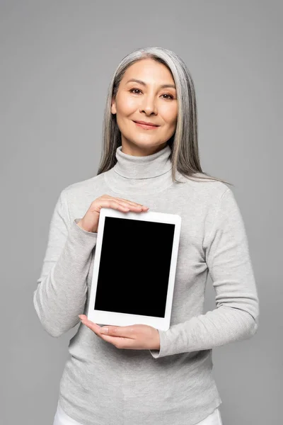 Happy attractive asian woman presenting digital tablet with blank screen isolated on grey — Stock Photo