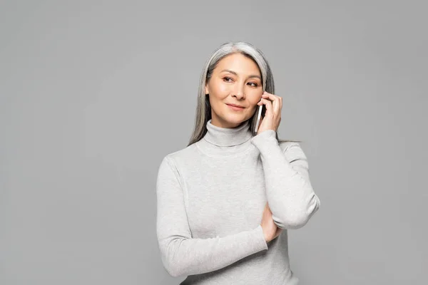 Asiatico donna in dolcevita con grigio capelli parlare su smartphone isolato su grigio — Foto stock