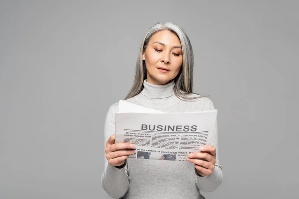 Adult asian woman in turtleneck with grey hair reading business newspaper isolated on grey — Stock Photo