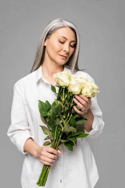 Adulto asiatico donna con grigio capelli tenere bouquet di bianco rose isolato su grigio — Foto stock