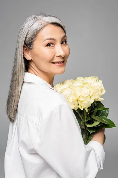 Adult asian woman with grey hair holding bouquet of white roses isolated on grey — Stock Photo