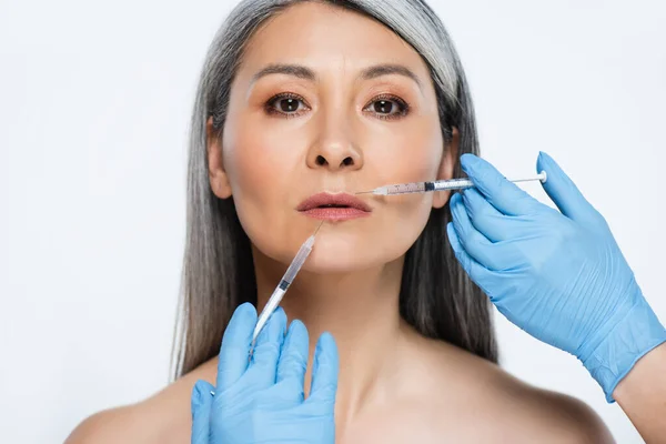 Обнаженная азиатка и врачи в латексных перчатках, держащие шприцы с инъекциями красоты, изолированными на сером — стоковое фото