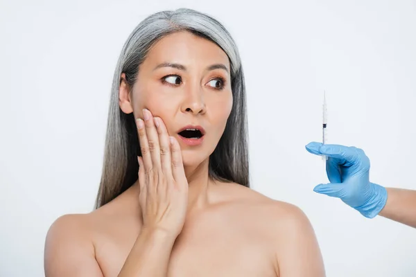 Sorprendido desnudo asiático mujer y doctor en látex guantes celebración jeringa con belleza inyección aislado en gris - foto de stock