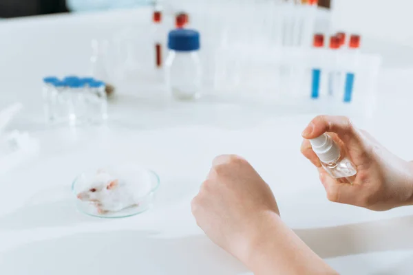 Cropped view of scientist spraying antiseptic on hands near test tubes and containers with medicines — Stock Photo