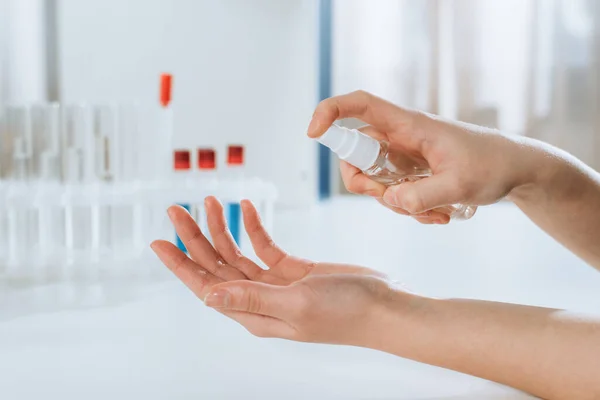 Cropped view of doctor spraying antiseptic on hands near test tubes — Stock Photo