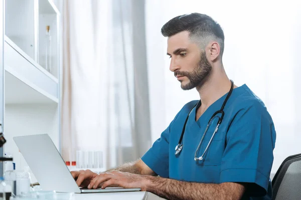 Young doctor with stethoscope on neck typing on laptop — Stock Photo