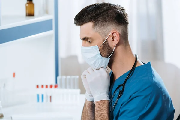 Young biologist in latex gloves fixing medical mask on face — Stock Photo