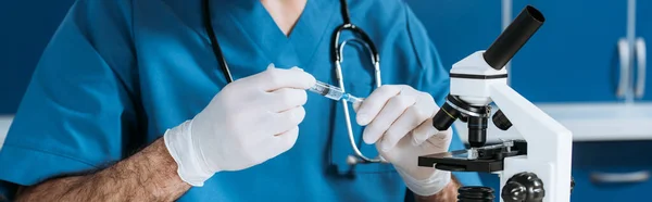 Cropped view of biologist in latex gloves holding syringe near microscope, panoramic shot — Stock Photo