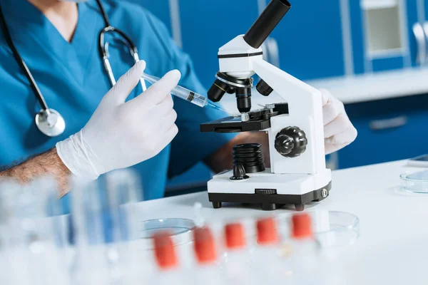 Cropped view of biologist in latex gloves holding syringe near microscope — Stock Photo