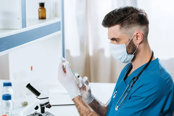 Молодой биолог в медицинской маске и латексных перчатках, принимающий лекарства со шприцем — стоковое фото