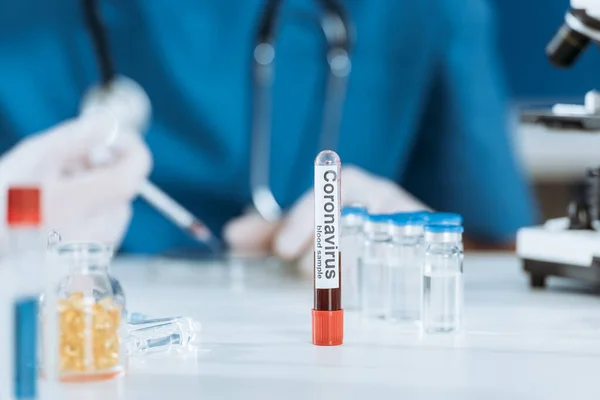 Selective focus of test tube with coronavirus inscription near scientist and glass containers with medicines — Stock Photo