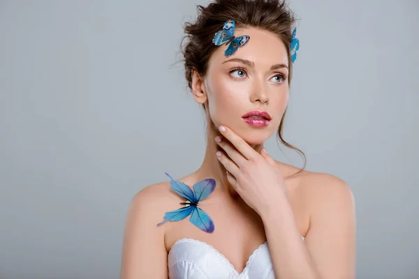 Belle jeune femme avec des papillons décoratifs touchant visage isolé sur gris — Photo de stock