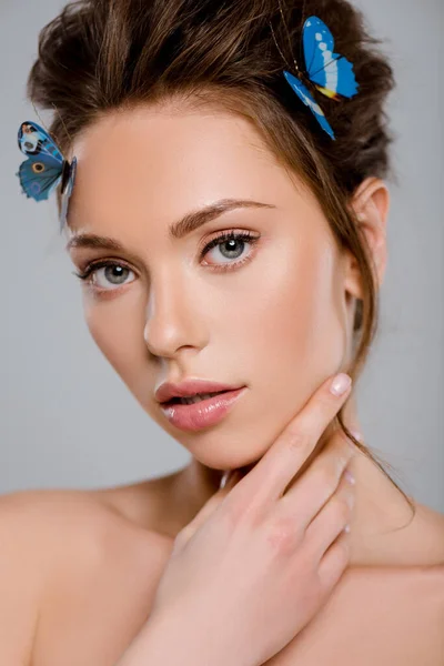 Красива дівчина з декоративними метеликами на обличчі, що торкається волосся, ізольована на сірому — стокове фото