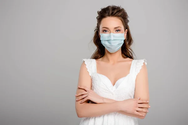 Jeune femme en masque médical debout avec les bras croisés isolés sur gris — Photo de stock