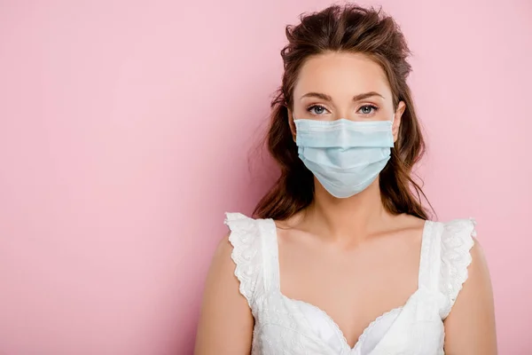 Jovem mulher em máscara médica de pé em rosa — Fotografia de Stock
