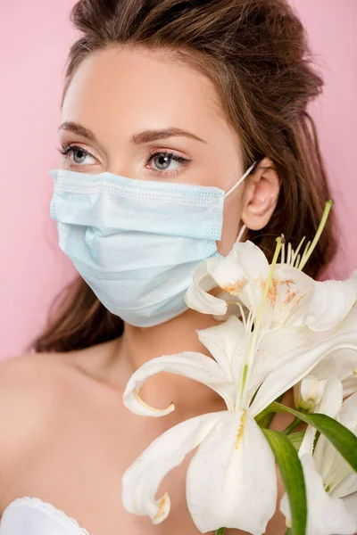 Giovane donna in maschera medica che tiene fiori isolati su rosa — Foto stock
