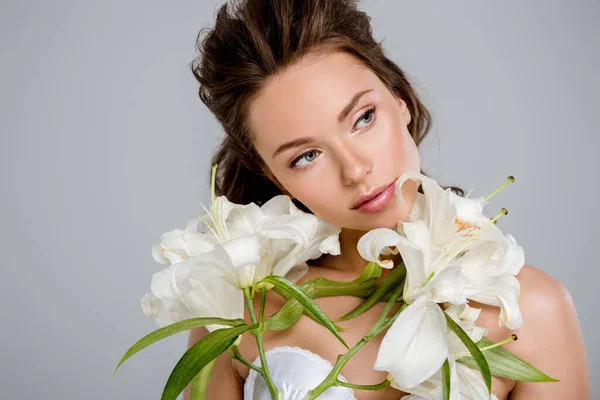 Молода красива жінка дивиться далеко біля білих квітів ізольована на сірому — стокове фото