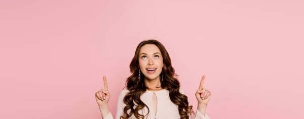 Plano panorámico de chica alegre señalando con los dedos y mirando hacia arriba aislado en rosa - foto de stock