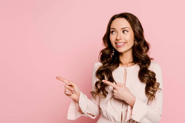 Feliz joven mirando hacia otro lado y señalando con los dedos aislados en rosa - foto de stock