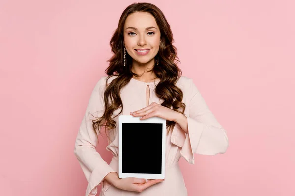 Fröhliche junge Frau hält digitales Tablet mit leerem Bildschirm isoliert auf rosa — Stockfoto