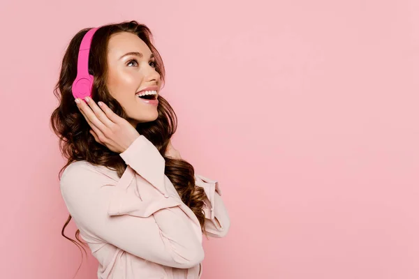 Mujer emocionada escuchando música en auriculares inalámbricos aislados en rosa - foto de stock