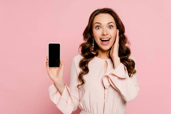 Aufgeregtes Mädchen hält Smartphone mit leerem Bildschirm und blickt isoliert auf Kamera in rosa — Stockfoto