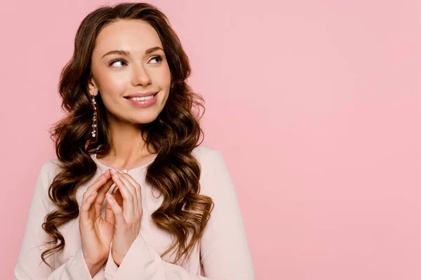 Mulher feliz com as mãos apertadas sorrindo e olhando para longe isolado em rosa — Fotografia de Stock