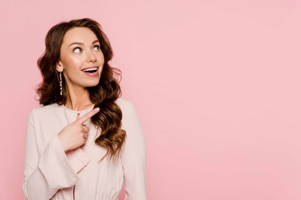 Excité femme pointant avec doigt et regardant loin isolé sur rose — Photo de stock