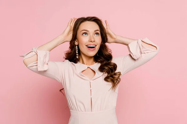 Excited young woman touching curly hair on pink — Stock Photo