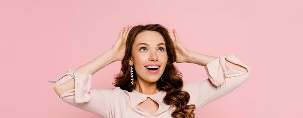 Plan panoramique de jeune femme excitée touchant les cheveux bouclés isolés sur rose — Photo de stock