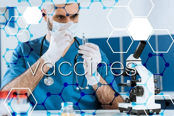 Enfoque selectivo del médico en máscara médica y guantes de látex mirando la ampolla con medicina cerca del microscopio, ilustración de vacunas - foto de stock