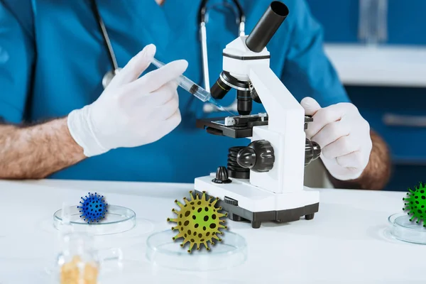 Cropped view of scientist in latex gloves holding syringe near microscope, bacteria illustration — Stock Photo