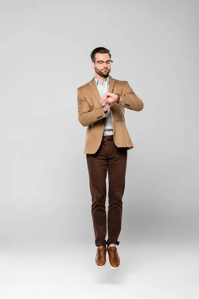 Handsome businessman levitating and looking at watch on grey — Stock Photo