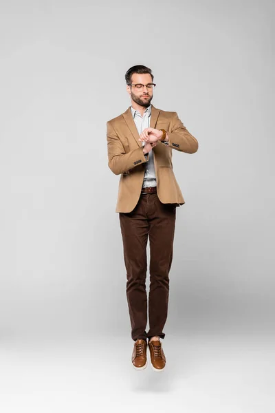 Bel homme d'affaires lévitant et regardant la montre sur gris — Photo de stock