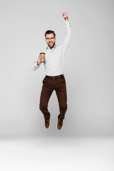 Hombre de negocios emocionado sosteniendo taza de papel mientras levita en gris - foto de stock