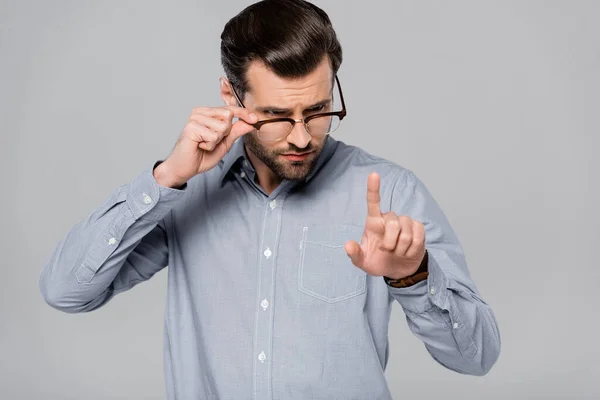 Schöner Geschäftsmann, der Brille anfasst und mit dem Finger auf Grau zeigt — Stockfoto