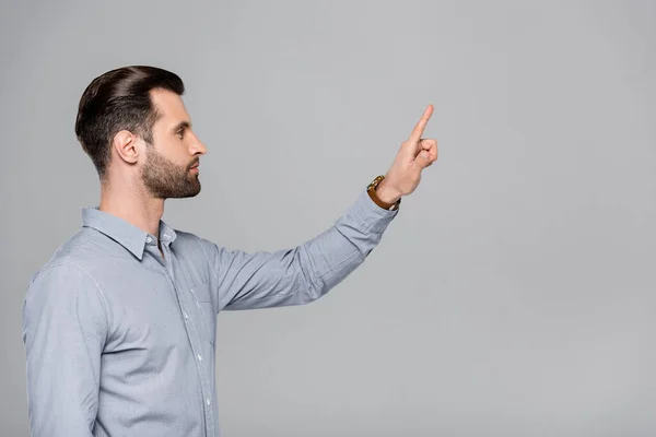 Vista lateral del hombre de negocios guapo señalando con el dedo aislado en gris - foto de stock