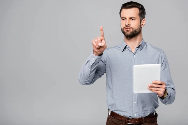 Guapo hombre de negocios señalando con el dedo y sosteniendo tableta digital aislado en gris - foto de stock