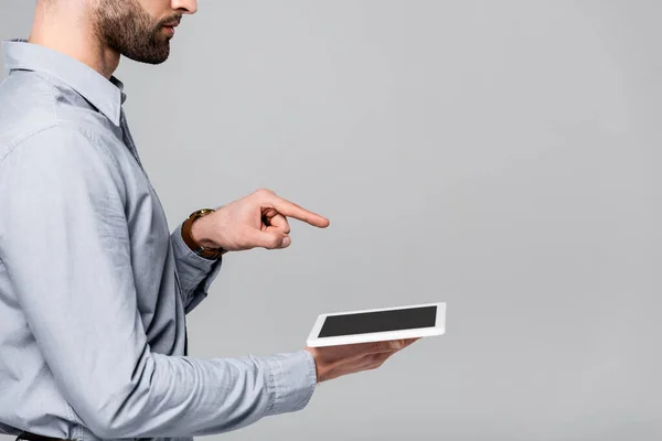 Обрізаний вид бізнесмена, який вказує пальцем і тримає цифровий планшет з порожнім екраном ізольовано на сірому — стокове фото