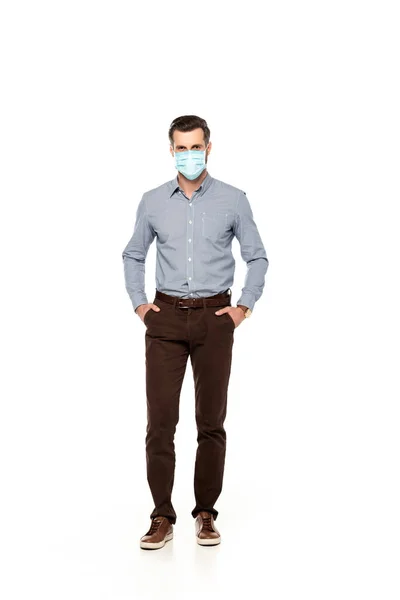 Hombre de negocios en máscara médica de pie con las manos en bolsillos aislados en blanco - foto de stock