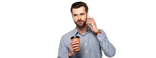 Plano panorámico de hombre guapo sosteniendo taza de papel y hablando en el teléfono inteligente aislado en blanco - foto de stock