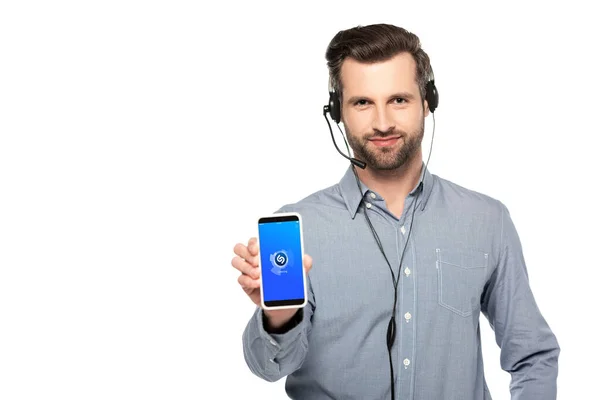 KYIV, UCRANIA - 23 de marzo de 2020: operador guapo en auriculares que sostiene el teléfono inteligente con la aplicación shazam en la pantalla aislada en blanco - foto de stock