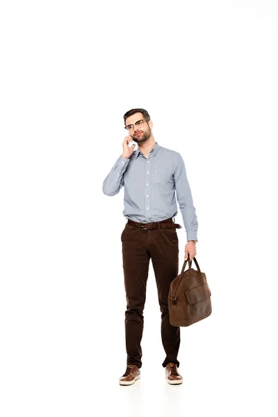 Guapo y barbudo hombre de negocios sosteniendo bolsa y hablando en el teléfono inteligente aislado en blanco - foto de stock