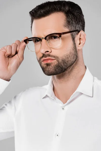 Barbudo y guapo hombre de negocios tocando gafas aisladas en gris - foto de stock