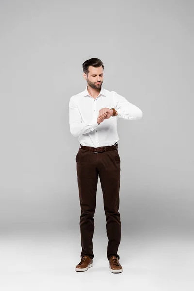 Handsome businessman in white shirt looking at watch on grey — Stock Photo