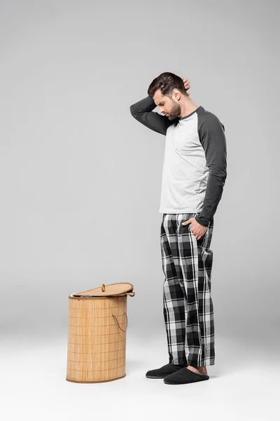 Homem barbudo olhando para cesta de roupa no cinza — Fotografia de Stock