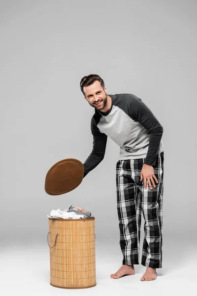 Bearded man smiling while standing near laundry basket on grey — Stock Photo