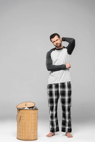 Cher homme toucher la tête tout en se tenant près panier à linge sur gris — Stock Photo