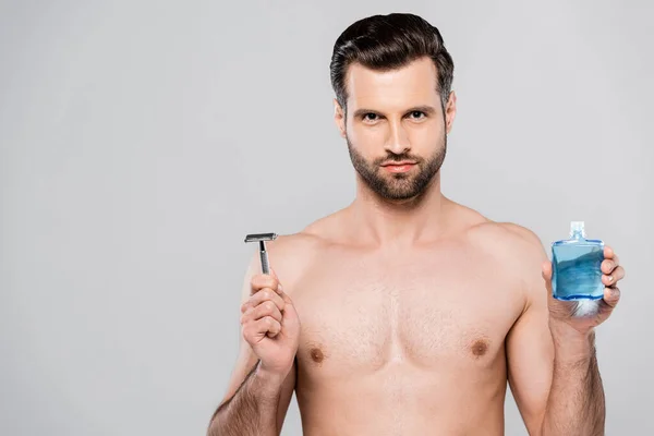 Bearded and muscular man holding after shave lotion and razor isolated on grey — Stock Photo